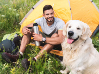 man sits in tent with yellow labrador dog in foreground